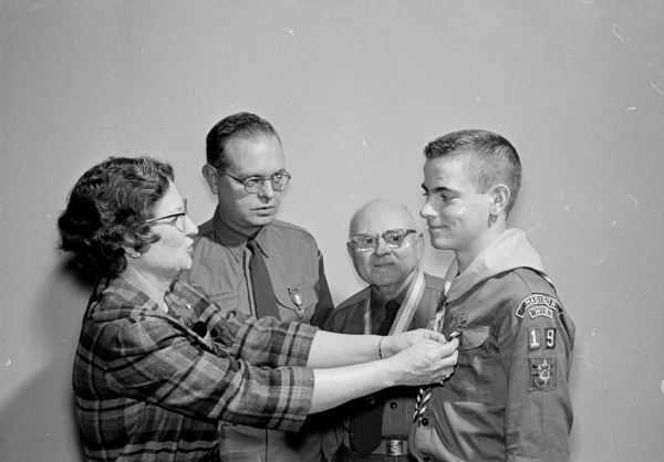 Catherine Moore pins the Eagle Scout badge on her son, Bill, at Luther Memorial Church. Bill's father, Wayne, who is the chairman of the troop, looks on with George Morris who made the presentation.