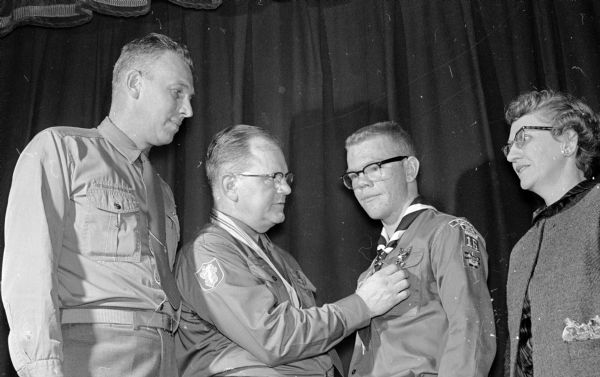 Ernest N. Wackwitz, Sr., scoutmaster of troop sixteen at Blessed Sacrament Catholic Church, pins an Eagle Scout badge on his son Ernest (Bud) Wackwitz, Jr. while district commissioner Miles F. Fenske and Bud's mother look on.