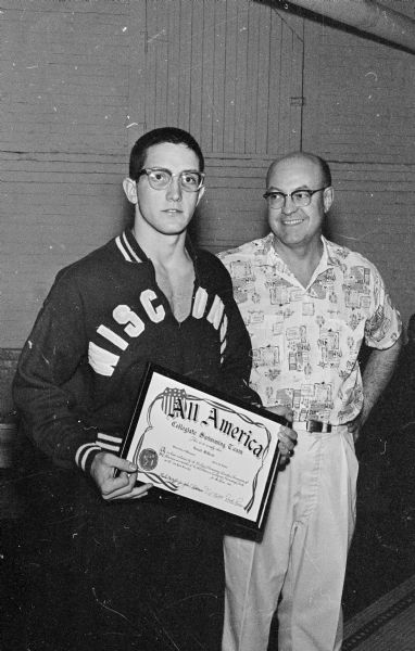 University of Wisconsin all-American swimmer Ron McDevitt holds his certificate from the 1960 NCAA swimming meet. Next to him is the University of Wisconsin swimming coach, John Hickman.