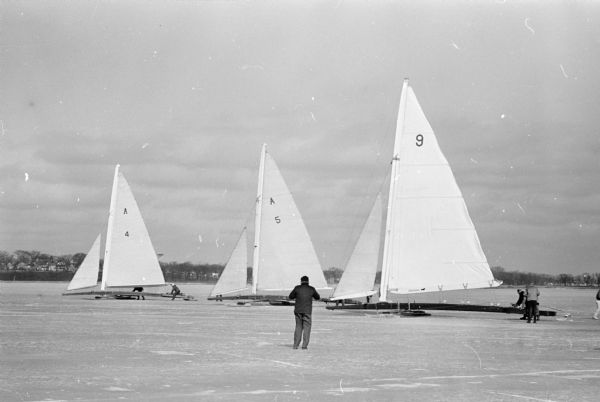A man is standing in front of iceboats on Lake Monona.