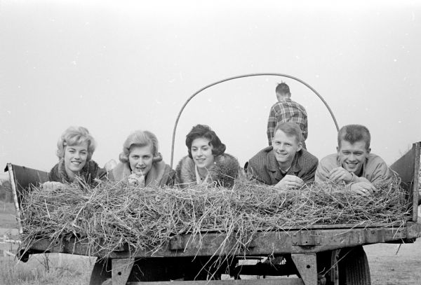 Five teenagers lying on the back of a horse-drawn hay rack at Grassman's Nob Hill Ranch on Old Middleton Road. The photograph was taken to advertise an upcoming Shorewood Hill Teen party. Plans include a supper, sleigh ride and a sock hop.