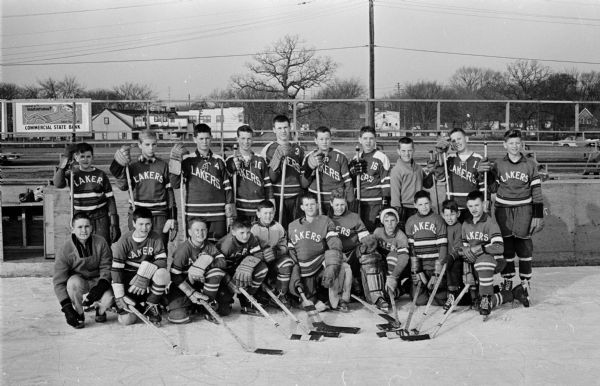 Outdoor group portrait of the Lakers hockey team who will be playing for the championship of the Wisconsin State Bantam Tournament. The members are shown in uniform, holding their hockey sticks.