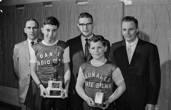 The Waunakee Midget Basketball League concludes its season with a potluck banquet and program. Holding the trophies are Lenny Bernards, left, of Dan's Radio and TV, and Art Barbian of the Waunakee State Bank team. Behind them are Don Oyan, coach of the Bank team; Ed Hellenbrand, league administrator; and Jerry Haugen, coach of Dan's Radio and TV.