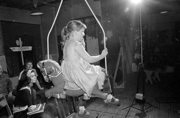 A young female cast member poses on a suspended merry-go-round horse as she watches a rehearsal of the musical show, "Carousel".