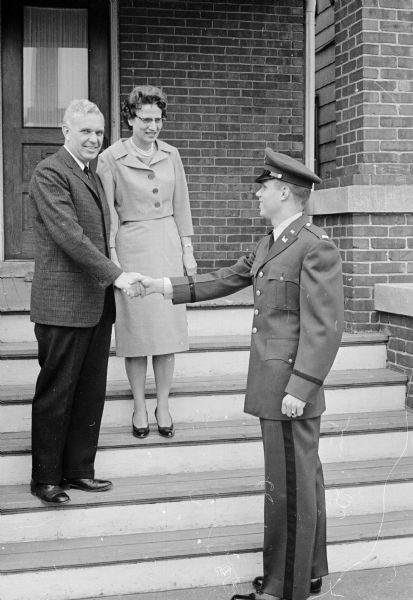 A young man wearing an army officers uniform shaking hands with his father and mother as they are posing on their porch steps at 616 E. Mifflin Street. At left is Henry E. Reynolds, mayoral candidate, shaking hands with his 22-year-old son, David Reynolds, a recent graduate of the University of Wisconsin and its four-year Reserve Officers Training Corps program. David Reynolds started his active duty service soon after wishing his parents "good luck and good bye."
