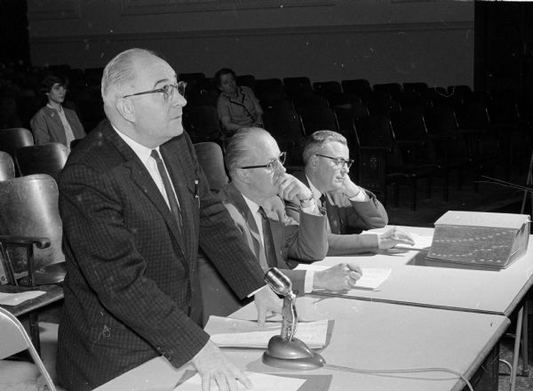 Officials gather at a table during the annual West High School spelling bee. At left is pronouncer Armand Ketterer. The two judges are George Blackman, principal of Crestwood school (center) and Paul Olson, principal of Midvale school.