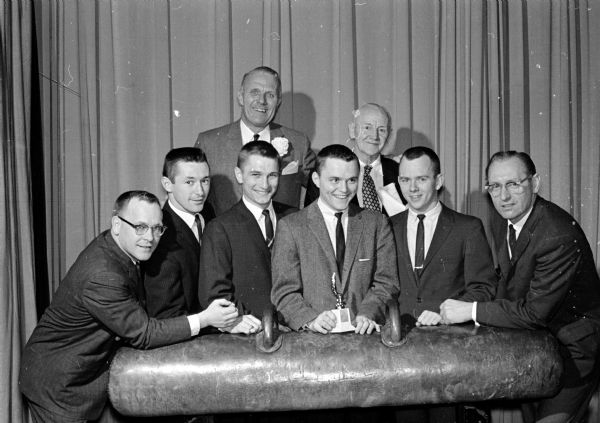 Madison Turners honor the University of Wisconsin gymnastics team at 8th annual banquet. Shown in the front row, left to right, are: Co-Coach Gordon Johnson, retiring Co-Capt. Clay Stebbins, Co-Capt. elect Jerry Klingbell, retiring Co-Capt. Jon Stillman, Co-Capt. elect Chuck Meyst, and Co-Coach George Bauer. Shown in back row, left to right, are: Bob Zimmerman, Wisconsin Secretary of State, and Bob Niemann, banquet organizer.