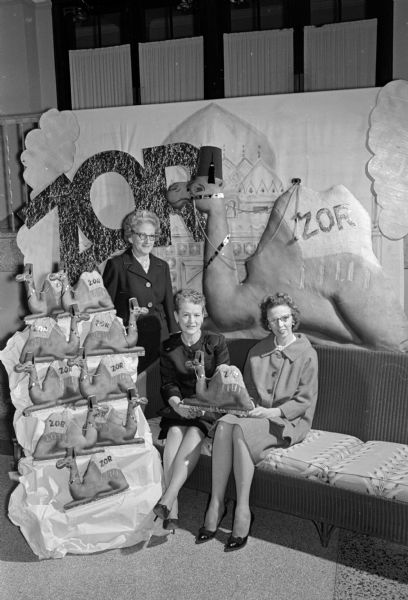 Three women sit next to a display of camels made by the decorating committee for the Zor Shrine's Potentate Ball. Edna Grant is in charge of decorations. Lucille Sachse is the wife of Zor Shrine potentate Earl Sachse. Alice Maloney is general chairman of the event.