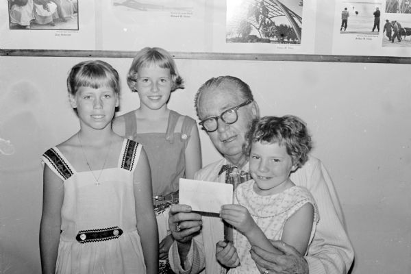 Group portrait of "Roundy" Coughlin, <i>Wisconsin State Journal</i> sports columnist, and three young girls who put on the play "Princess and the Pea" to collect money for "Roundy's Fun Fund." The girls are, left to right, Deborah Niebuhr, Barbara Niebuhr and Debra Alldredge.