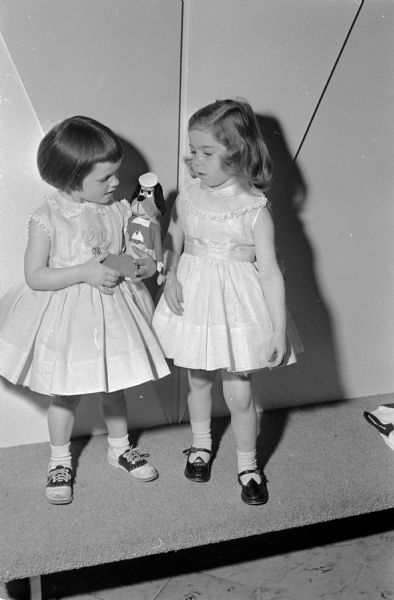 Two small girls, one holding a toy, modeling spring dresses and shoes in preparation for the spring style show. The Opti-Mrs. Club of Middleton sponsored the show to raise money for a nursing scholarship for a Middleton High school girl. The little girls are Linda Kath and Suzanne Sphar.