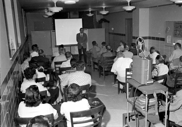 Dr. Richard Thurrell, psychiatrist, stands at the front of a classroom in Mendota State Hospital trading ideas with a group of patients who are alcoholics.