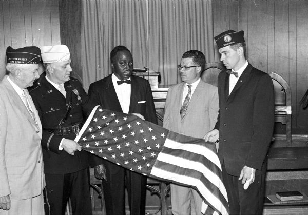 The Madison chapter of the Disabled American Veterans presents a 50-star flag in honor of John Parrish, center, a member of the newly built Mt. Zion Church at 2021 Fisher Street. Parrish was a former commander and treasurer of the Madison D.A.V. chapter, a veteran of  World War II, and was active in Madison and state veterans organizations.  Displaying the flag are, left to right, R. J. Koelsch, past chapter commander; Charles Peckham, chapter commander; Parrish; the Rev. Joe Dawson, pastor of the church; and Richard Doll, senior vice commander. The other three men are wearing veterans hats.
Parrish was a former commander and treasurer of the Madison D.A.V. chapter, a veteran of World War II, and was active in Madison and state veteran’s organizations. Parrish worked for the US Armed Forces Institute and then Forest Products Laboratory, but he is best remembered in Madison for decades spent volunteering at the William S. Middleton Memorial Veterans Hospital., where he visited with patients.