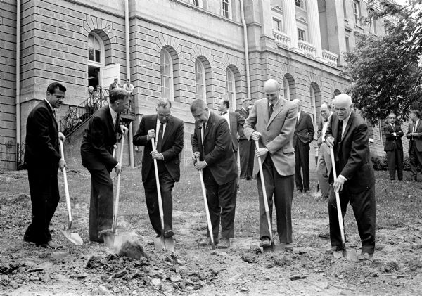 Men hold shovels during the groundbreaking ceremony held for the new U.W. mathematics building. It will be located between Bascom Hall and Sterling Hall and named Van Vleck Hall. Shown breaking ground are, (from left): Joseph Flad, Flad and Associates, building architect; Dean John Willard, U.W. Graduate School; A.W. Peterson, U.W. vice president of business and finance; Karl Yasko, state architect; Prof. S.C. Kleene, chairman of U.W. Department of Mathematics; and Dean Mark H. Ingraham, U.W. Letters and Science.