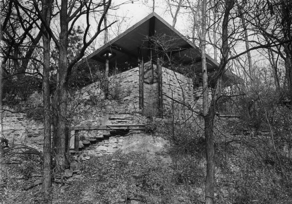 Exterior view of a house, named "Ode to an Oak Leaf" by its architect James Dresser, and built in 1950 in the style of Frank Lloyd Wright (Dresser was a pupil of Wright). Designed in the Wright style, shaping to fit the natural terrain-even going so far as to cut a hole through the roof to let a tree grow through. The house, located at 1002 Oak Way in Shorewood Hills, was built using stone from an old quarry on the building site.
