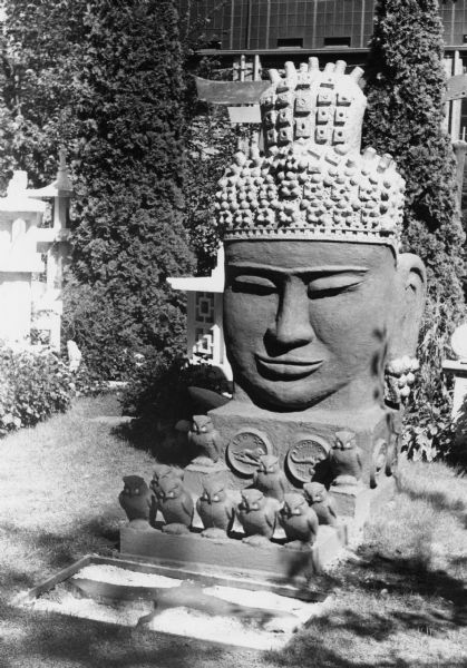 12-foot-high Cambodian warrior head sculpture in the garden at 237 Waubesa Street. It was made from concrete by the artist Sydney Boyum. Many of his scuptures are now on public display in the Marquette Street neighborhood.