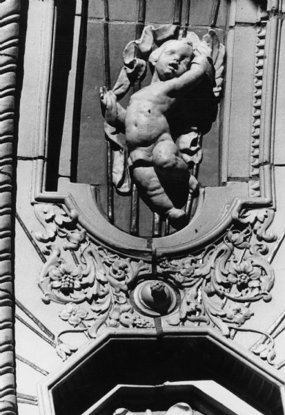 A cherub is the central focus of this detail of the richly decorated facade of Edgewood High School at 2219 Monroe Street. Other features in the facade include swirled pillars, miniature balconies, and angel heads and wings.