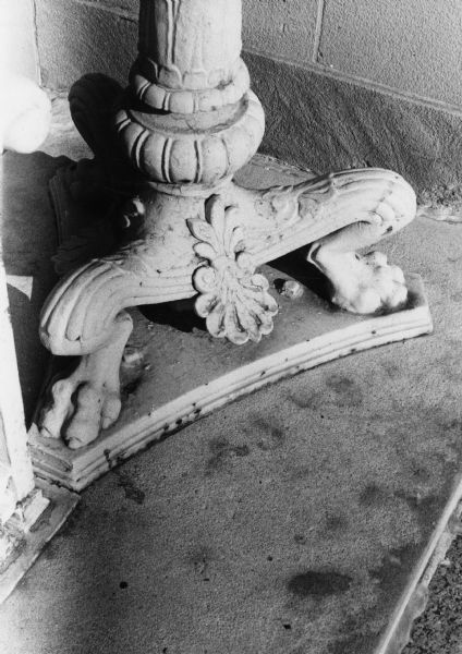 The base of a lamp post formed in the shape of crouched legs and feet. The lamp post is at the old main Post Office/Madison Municipal Building, 215 Monona Avenue (Martin Luther King, Jr. Boulevard as of January 19, 1987).