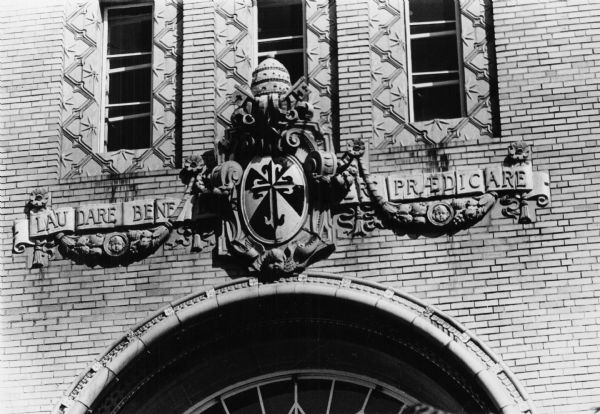 An elaborate cartouche above the main entrance to Edgewood High School, constructed in 1927, at 2219 Monroe Street. The Latin inscription translates to "To praise, to bless, to preach".