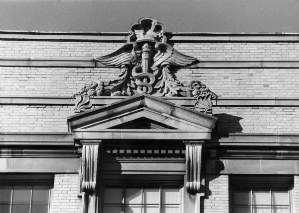 A carved caduceus, which is a mythological winged staff with intertwined serpents, decorates the entrance to a wing of old Wisconsin General Hospital (1924-1979), 1300 University Avenue on the University of Wisconsin-Madison campus.