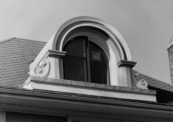 A dormer window on a house at 956 Spaight Street. The window is framed by carefully carved wooden volutes (Greek spiral scrolls) and concentric arches.