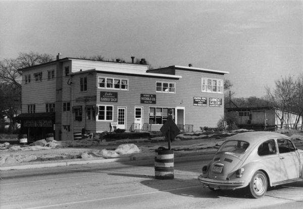 Exterior view of the Shorewood Shopping Center, which included the businesses Jack's Shorewood Barber Shop, Downhill Ski Center, and Beautiful People Modeling School & Agency. The building was demolished in 1979.