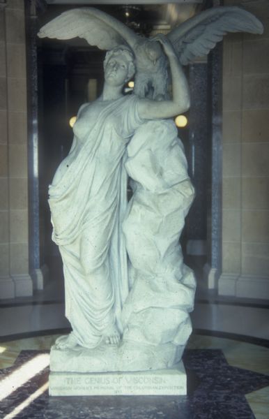 "Genius of Wisconsin" statue, which was originally sculpted by Helen Mears for the Columbian Exposition of 1893. It was later recreated in marble by the Piccirilli Brothers and funded by women of Wisconsin. It now stands at the first floor southeast entrance of the Wisconsin State Capitol.