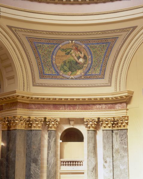 "Liberty" pendentive, one of four panels of glass mosaic by Kenyon Cox, in the Wisconsin State Capitol. The artist sought the decorative properties of the Byzantine mosaics, while creating a style more in harmony with the purely Beaux-Arts character of the building. Located between the four arches in the rotunda, the pendentives make the transition from the octagonal form of the rotunda to the circular form of the dome. Each pendentive has a colossal seated figure on a gold background, which symbolize the three divisions of the powers of the state--the legislative, the executive, and the judicial. The last represents liberty, the foundation of all power in a free country.
