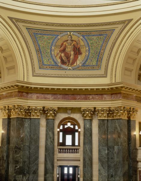 "Government" pendentive, one of four panels of glass mosaic by Kenyon Cox, in the Wisconsin State Capitol. The artist sought the decorative properties of the Byzantine mosaics, while creating a style more in harmony with the purely Beaux-Arts character of the building. Located between the four arches in the rotunda, the pendentives make the transition from the octagonal form of the rotunda to the circular form of the dome. Each pendentive has a colossal seated figure on a gold background, which symbolize the three divisions of the powers of the state--the legislative, the executive, and the judicial. The last represents liberty, the foundation of all power in a free country.