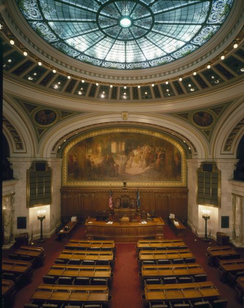 Assembly Chamber, in the Wisconsin State Capitol, before restoration in 1988. Above the skylight can be seen long fluorescent light fixtures which are no longer there. After restoration the lighting was hidden.