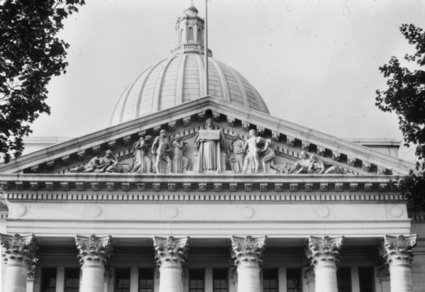 North Pediment, called "Learning of the World, by the sculptor Attilio Piccirilli. This is one of four groups of granite statuary on the exterior of the Wisconsin State Capitol. The central figure is holding a tablet on which is written the inscription "Sapientia" (Wisdom), representing Enlightenment.