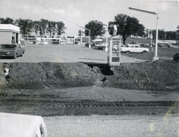 Standard Oil station with road work taking place in the foreground. Included in the view is a telephone booth.