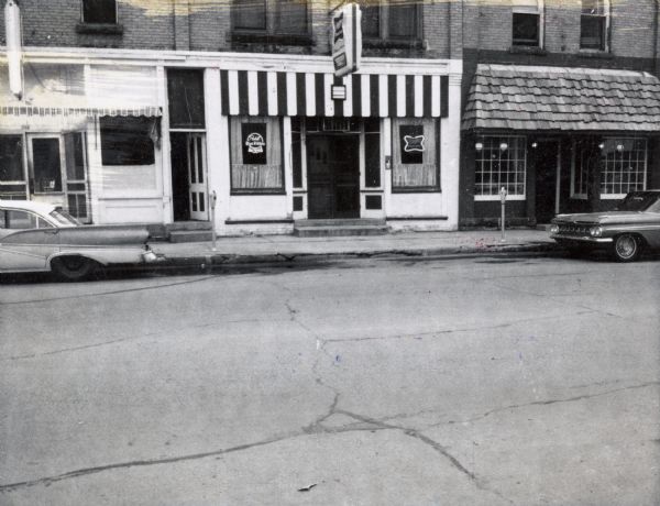 A row of three storefronts along State Highway 21 & 73 in Wautoma, Wisconsin.  One store front is clearly a bar; a second, whose original front has been greatly altered, may be a bar or a restaurant.