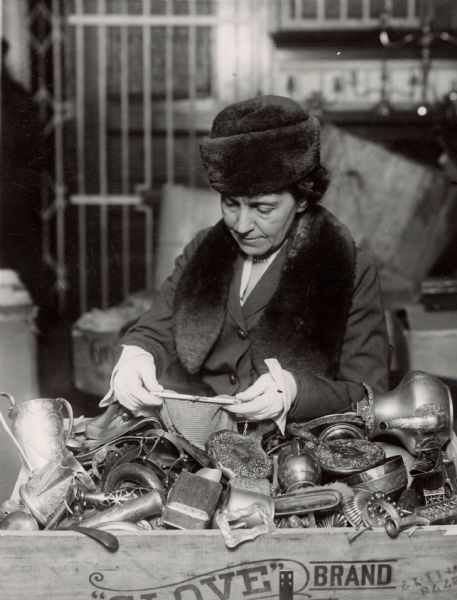 Mrs. William Bartlett of the Aviation Committee of the National Special Aid Society, examines metal objects donated by members to be sold to benefit American aviators during World War I.