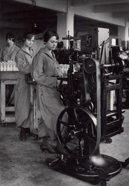 A World War I female factory worker dressed in a uniform repairing her own machinery.