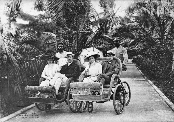 Two couples are shown seated in rickshaw-like carriages pushed by men on bicycles in Palm Beach, California.