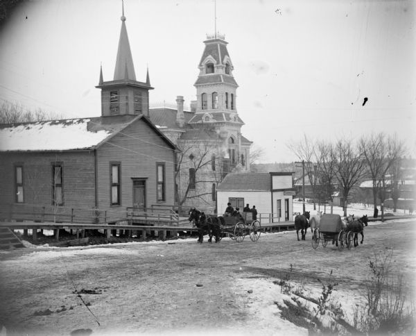 Horse and carriages passing in front of the Baptist Church, the Jackson County Courthouse, and the dentist office of R.C. Gebhardt.