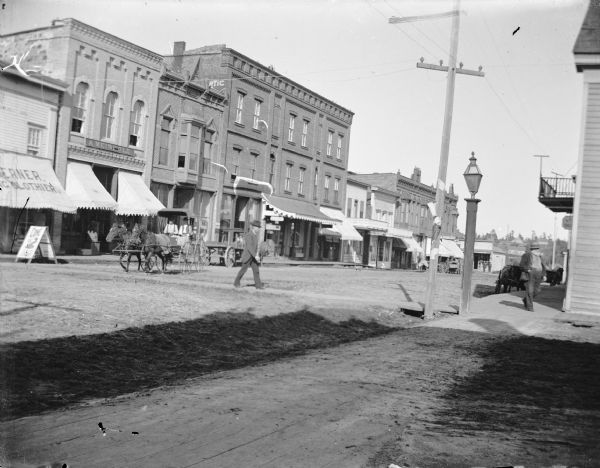 Buildings on the southwest section of Main Street at the intersection of Main and First Streets. Storefronts, from left to right, include A.F. Werner, A. Meinhold. Men are walking on the sidewalk and crossing Main Street.