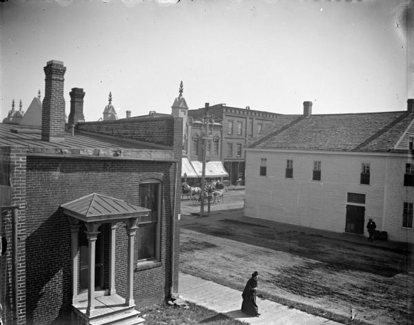 Elevated view of woman walking along side street of town. In the background are horses and carriages.
