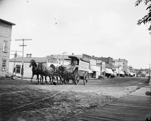Man driving flour mill wagon pulled by a team of two horses. Wagon reads "Hixton Mills" and "Baron Amond Flour".