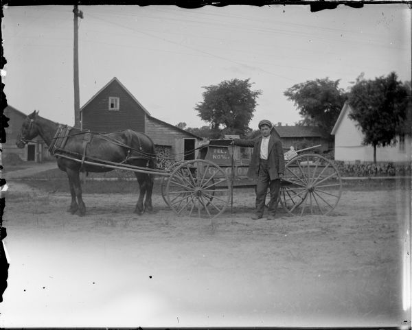 Boy posing standing next to a delivery wagon pulled by a single horse. Marked on side "Tel. 76" and a box of "Saxon Oats" in the wagon.
