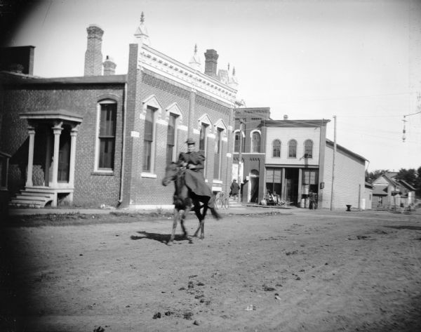 Woman riding sidesaddle through town. Storefront on the northwest corner of Main and First Streets is P.L. Moe & Company Hardware.
