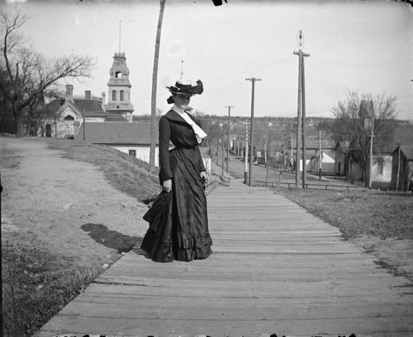 Woman posing standing on a board sidewalk on the hill of Main Street.