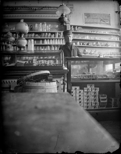 Interior of a store with a clerk standing behind a cigar counter. Man behind the counter identified as probably Oliver Olson.