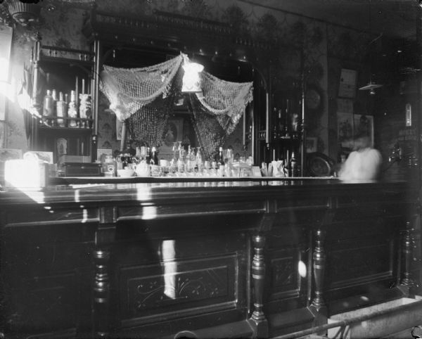 Interior of a tavern showing a bar and back counter, and a blurred individual moving behind the bar on the right.
