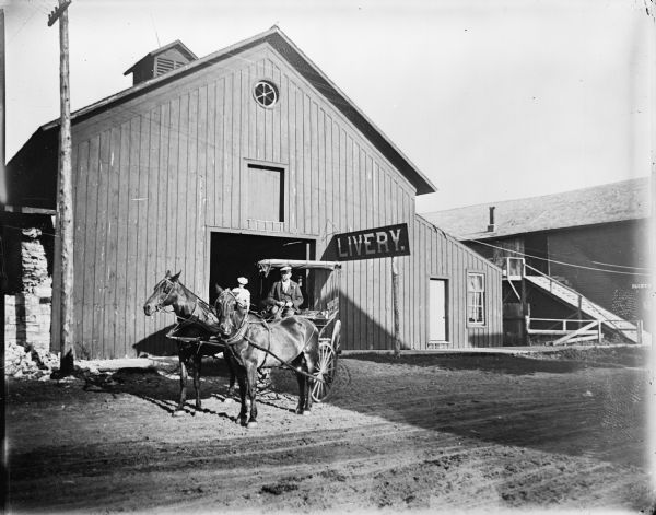 Man driving team and wagon from livery stable. On the right is a ramp at the side of a building, which possibly leads to the paint shop owned by John Gruber.