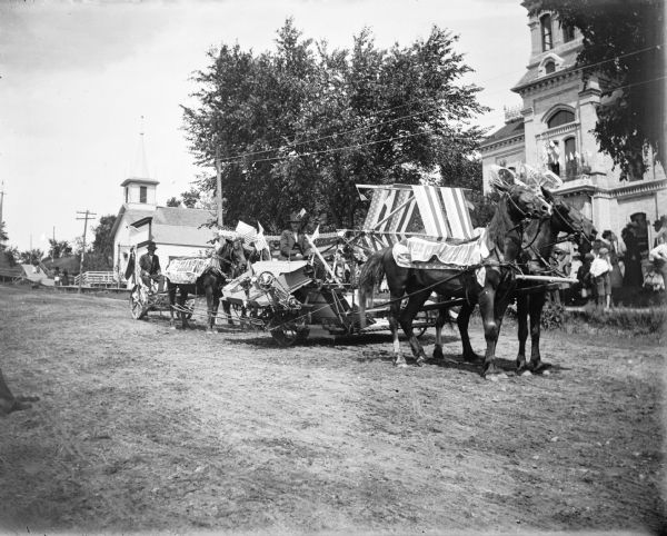 Farm equipment, probably from the Champion Company, and horses patriotically decorated and passing the Baptist Church and the Jackson County Court house.