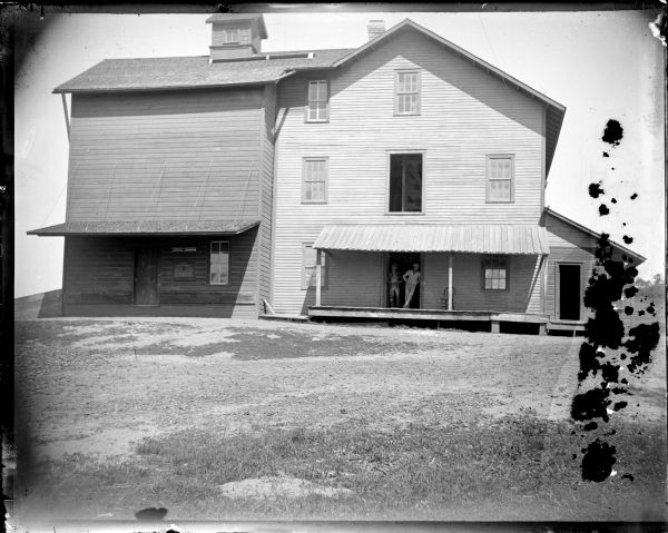Two men leaning in the doorway of a three-store building, possibly John Dunn's Mill.