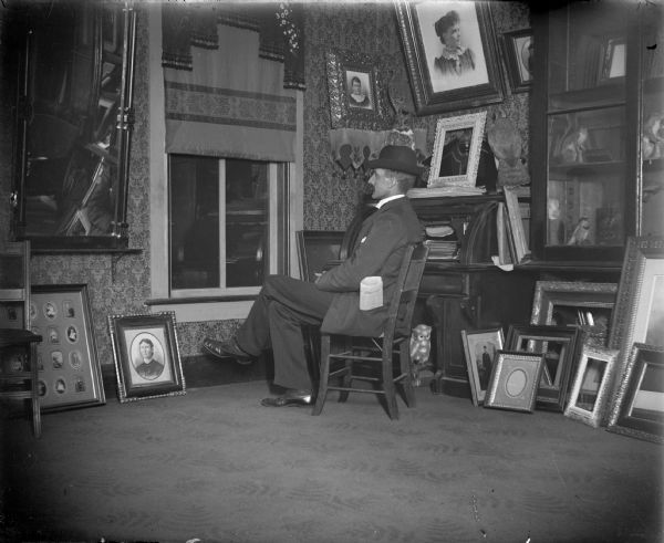 Man, probably Charles J. Van Schaick, looking out a window, probably from inside the Van Schaick studio, surrounded by portraitures and frames. In his left pocket is a Chicago newspaper.