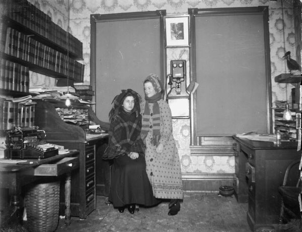Bundled women seated in front of a roll-top office desk, possibly the office of John Forbes over the old Fire Hall. A typewriter on the table and a telephone on the wall.
