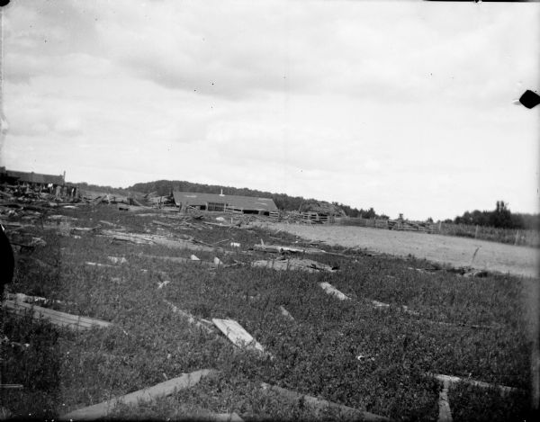 Debris of wood and board scattered around a field, probably due to a tornado. Group of people in the distance on the left side of the image.